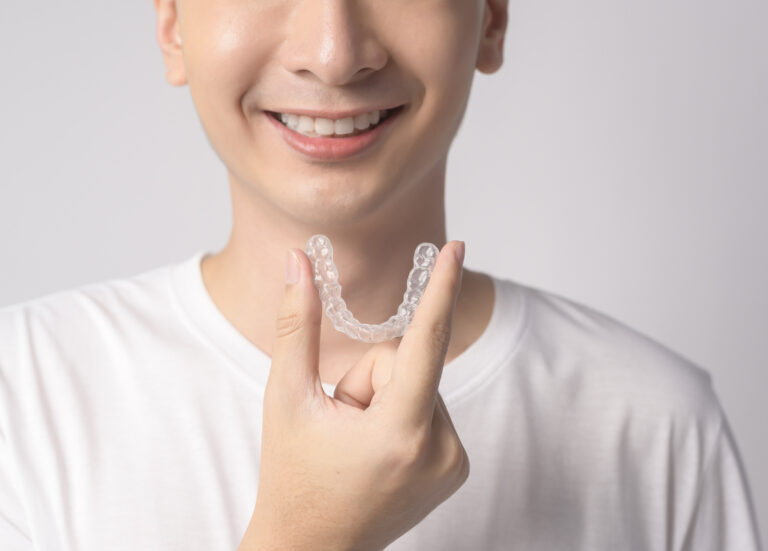 close up of smiling boy holding clear aligner